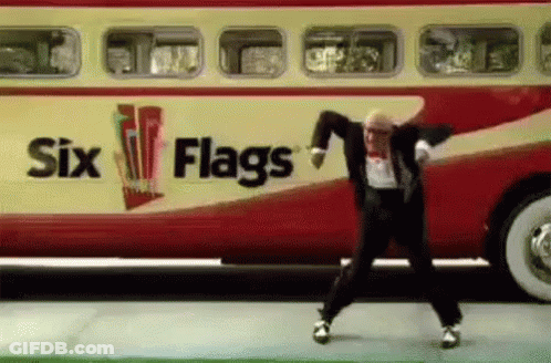 A Man In A Suit Is Dancing In Front Of A Bus That Says Six Flags . GIF