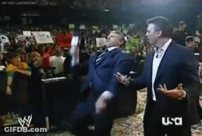 A Man In A Suit Is Dancing In Front Of A Crowd While A Man In A Suit Talks To Him .. GIF