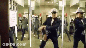 A Man In A Suit Is Dancing In Front Of A Mirror While Wearing A Hat With The Letter S On It GIF