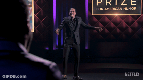 A Man In A Suit Is Dancing In Front Of A Prize For American Humor Sign GIF