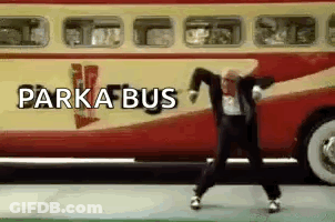A Man In A Suit Is Dancing In Front Of A Red And Yellow Bus . GIF