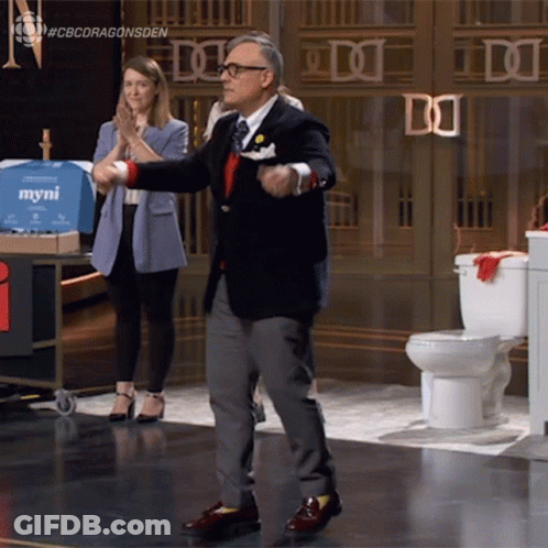 A Man In A Suit Is Dancing In Front Of A Sign That Says Myni On It GIF