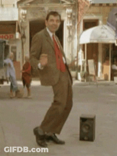 A Man In A Suit Is Dancing On A Sidewalk In Front Of A Store That Says Mop GIF