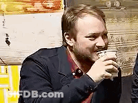 A Man In A Suit Is Drinking A Cup Of Coffee . GIF