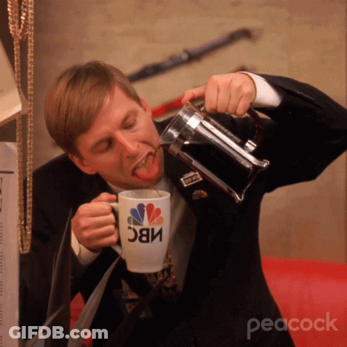 A Man In A Suit Is Drinking From A Nbc Coffee Mug GIF