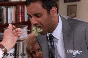 A Man In A Suit Is Eating A Piece Of Lettuce With A Fork .. GIF