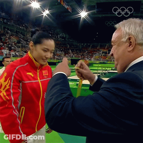 A Man In A Suit Is Giving A Medal To A Woman In A Red And Yellow Jacket GIF
