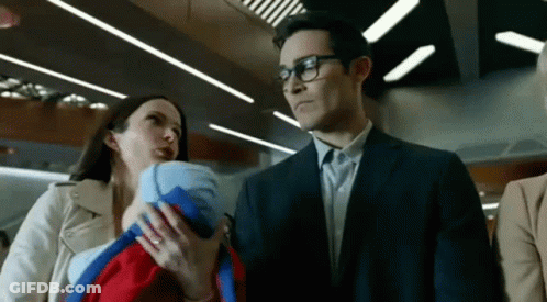 A Man In A Suit Is Holding A Baby While A Woman Holds A Baby In Her Arms . GIF