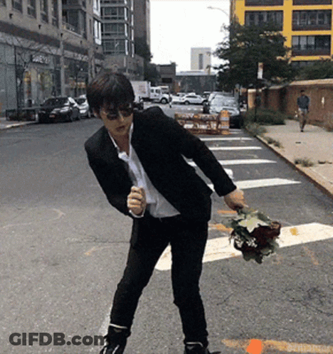 A Man In A Suit Is Holding A Bouquet Of Flowers In His Hand GIF