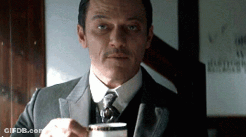 A Man In A Suit Is Holding A Cup Of Coffee GIF