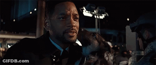 A Man In A Suit Is Holding A Dog In His Arms . GIF
