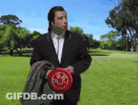 A Man In A Suit Is Holding A Frisbee In A Park With Trees In The Background GIF