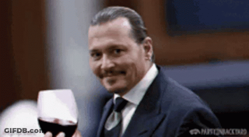 A Man In A Suit Is Holding A Glass Of Red Wine . GIF