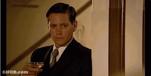 A Man In A Suit Is Holding A Glass Of Wine GIF