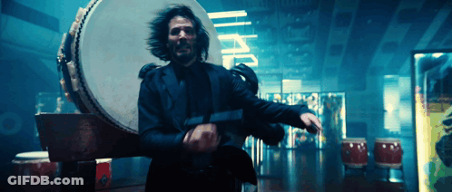 A Man In A Suit Is Holding A Gun In Front Of A Drum And A Sign That Says I.p.p. GIF