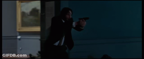 A Man In A Suit Is Holding A Gun In Front Of A Statue GIF