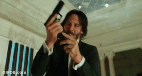 A Man In A Suit Is Holding A Gun In His Hand GIF