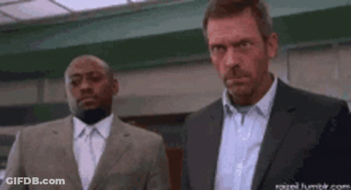 A Man In A Suit Is Holding A Large Knife While Another Man Stands Behind Him . GIF