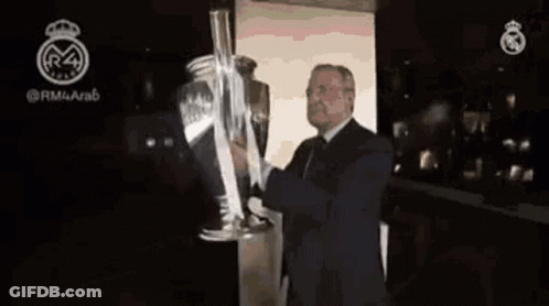 A Man In A Suit Is Holding A Large Trophy In His Hands . GIF