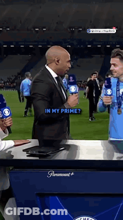 A Man In A Suit Is Holding A Microphone And Talking To Another Man In A Blue Shirt . GIF