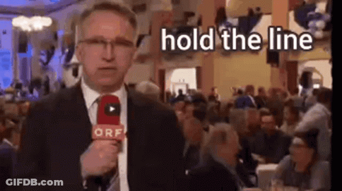 A Man In A Suit Is Holding A Microphone In Front Of A Crowd . GIF