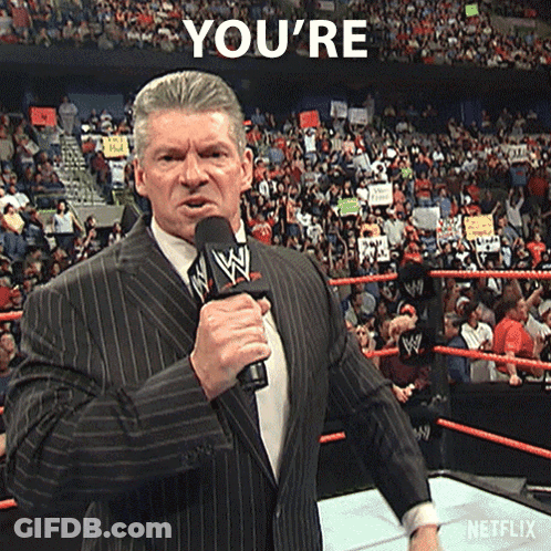 A Man In A Suit Is Holding A Microphone In Front Of A Crowd And Says You 'Re In The Background GIF