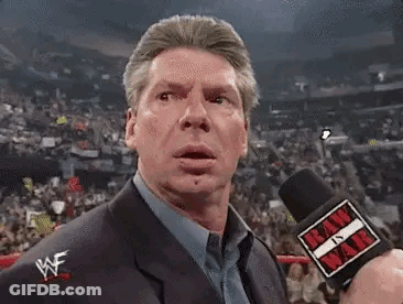 A Man In A Suit Is Holding A Microphone In Front Of A Crowd Of People . GIF