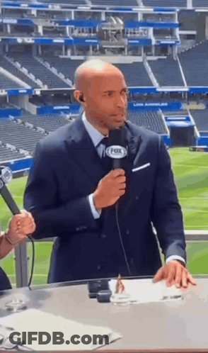 A Man In A Suit Is Holding A Microphone In Front Of A Fox Stadium . GIF