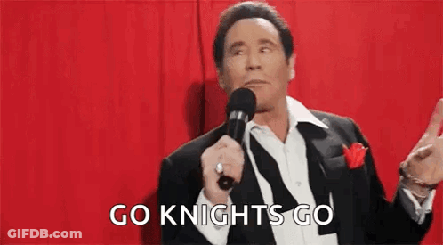 A Man In A Suit Is Holding A Microphone In Front Of A Red Curtain . GIF