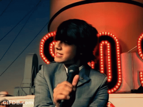 A Man In A Suit Is Holding A Microphone In Front Of A Sign That Says ' Co ' GIF