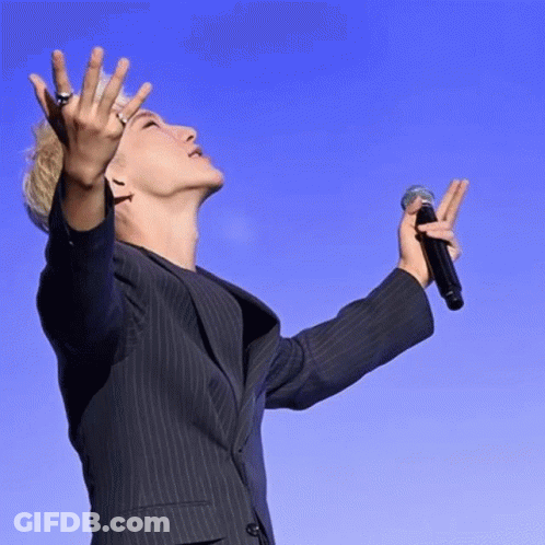 A Man In A Suit Is Holding A Microphone In His Right Hand GIF