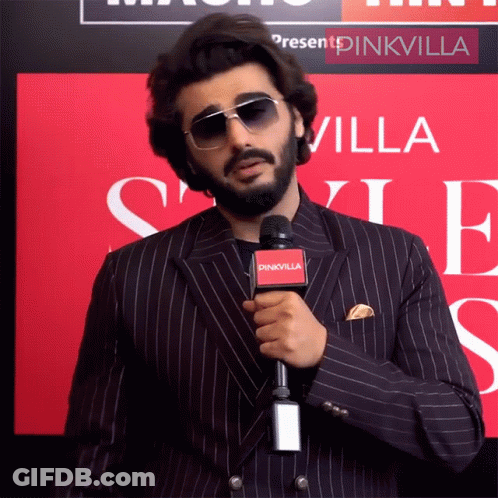 A Man In A Suit Is Holding A Microphone That Says Pinkvilla On It GIF