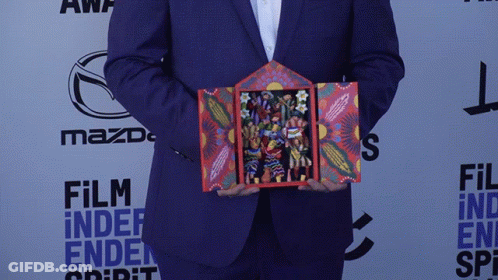 A Man In A Suit Is Holding A Painting In Front Of A Mazda Logo GIF