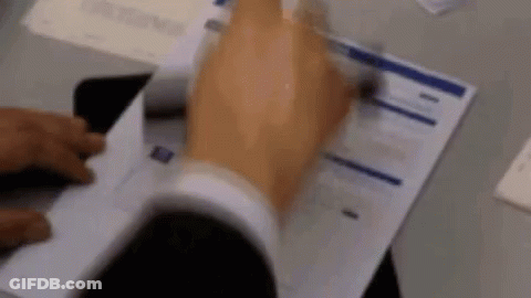 A Man In A Suit Is Holding A Piece Of Paper In His Hand . GIF