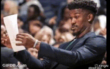 A Man In A Suit Is Holding A Piece Of Paper In His Hands . GIF