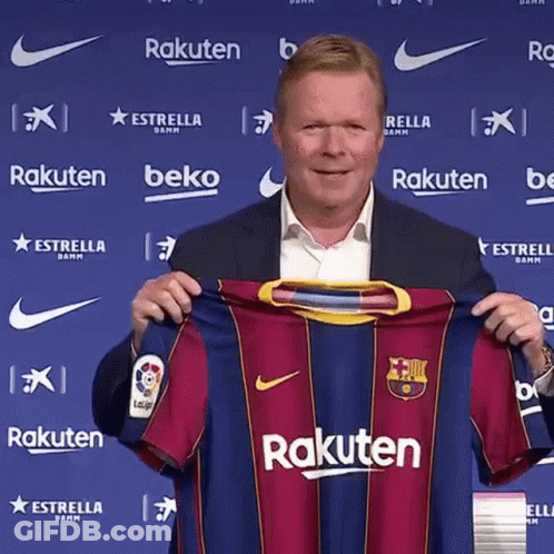 A Man In A Suit Is Holding A Rakuten Jersey In Front Of A Blue Wall . GIF
