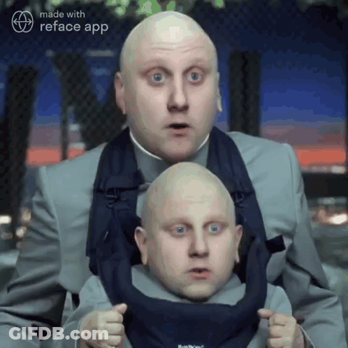 A Man In A Suit Is Holding A Smaller Man In A Baby Carrier .. GIF