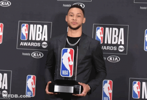 A Man In A Suit Is Holding A Trophy In Front Of A Wall That Says Nba GIF