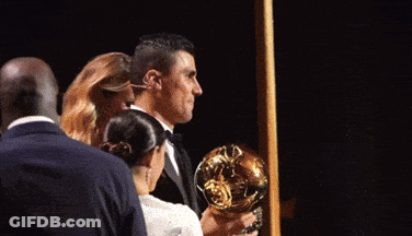 A Man In A Suit Is Holding A Trophy In His Hands GIF