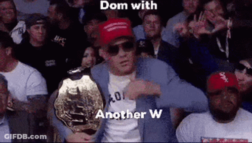 A Man In A Suit Is Holding A Ufc Championship Belt In Front Of A Crowd . GIF