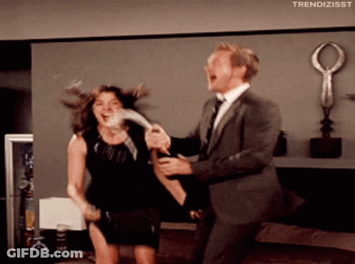 A Man In A Suit Is Holding A Woman In A Black Dress Who Is Laughing GIF
