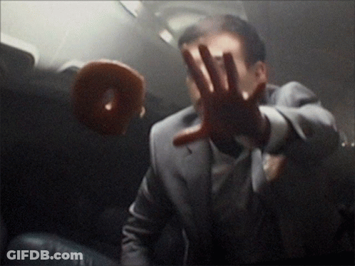 A Man In A Suit Is Holding His Hand Up In Front Of A Doughnut GIF