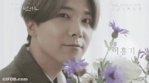 A Man In A Suit Is Holding Purple Flowers In Front Of His Face .. GIF
