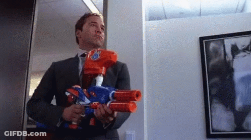 A Man In A Suit Is Holding Two Nerf Guns . GIF