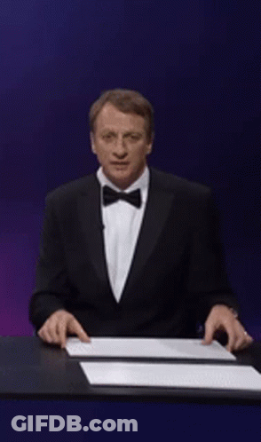 A Man In A Suit Is Holding Up A Sign That Says Tony Hawk GIF