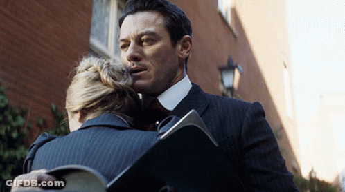 A Man In A Suit Is Hugging A Woman Who Is Holding A Folder GIF