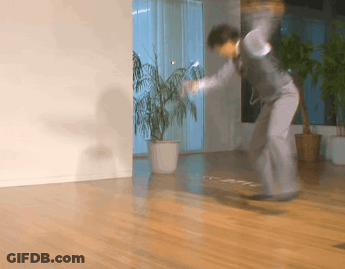 A Man In A Suit Is Jumping In A Room With A Plant In A Pot GIF