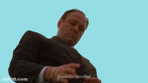 A Man In A Suit Is Kneeling In Front Of A Fence With A Green Dragonbot Watermark GIF