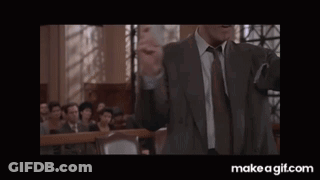 A Man In A Suit Is Laughing In A Courtroom While Holding Something In His Hands . GIF