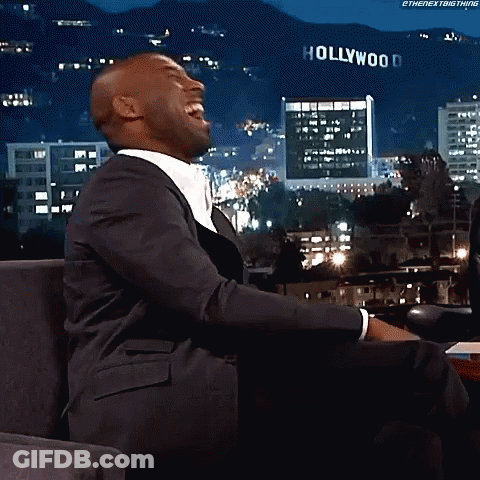 A Man In A Suit Is Laughing In Front Of A Sign That Says Hollywood GIF